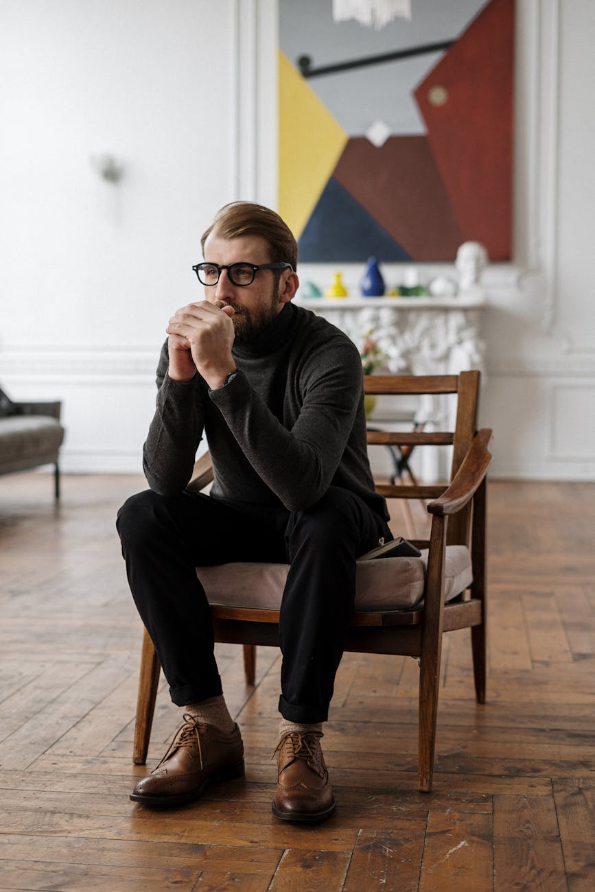 Woman in Gray Long Sleeve Shirt and Black Pants Sitting on Brown Wooden Armchair